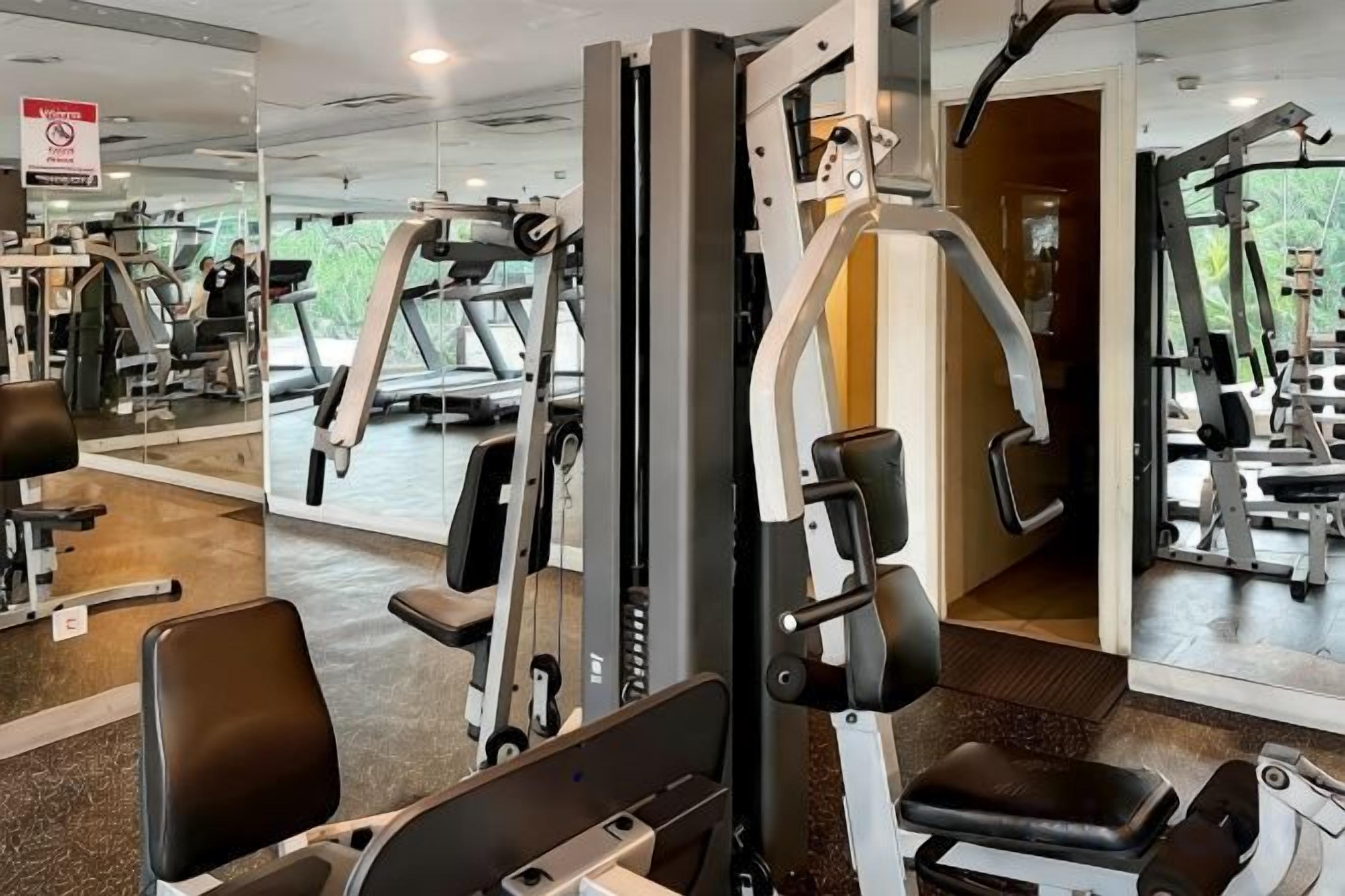 A gym with various exercise machines, mirrors, and a seating area.