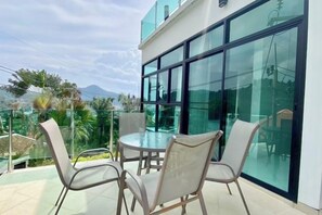 Un espace extérieur moderne, aménagé avec une table et des chaises en verre, offrant une vue sur une montagne et la verdure environnante.