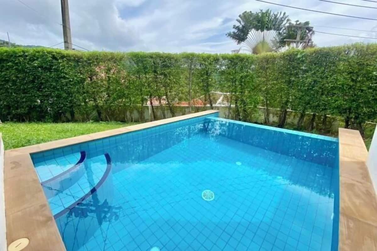 A rectangular swimming pool with blue tiles, surrounded by a low hedge and a grassy area.