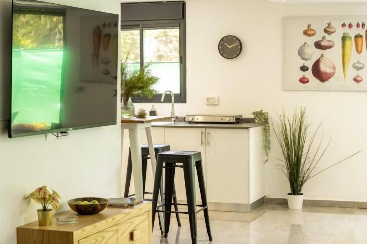 A modern kitchen with a TV, bar stools, and a clock on the wall.