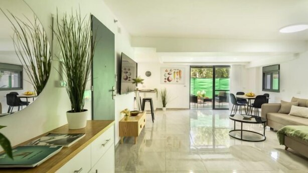 A modern living room with a sofa, a dining table, and a kitchen area with cabinets and a countertop. - Bahai Gardens Serenity Apartment (Haifa)