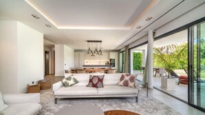 A modern living room with a sofa, coffee table, and a view of the kitchen and outdoor area. - All About Villa Gardenias (Marbella)