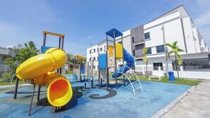 A playground with slides and climbing structures, surrounded by a building with a modern design. - 28 RESIDENCE-R13 (Sepang)