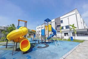 A playground with slides and climbing structures, surrounded by a building with balconies. - 28 RESIDENCE-R13 (Sepang)