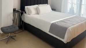 A modern hotel room with a large bed, bedside tables, a small seating area, and a window with curtains.