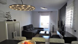 A modern living room with a sofa, a dining table with a fruit bowl, and a TV.