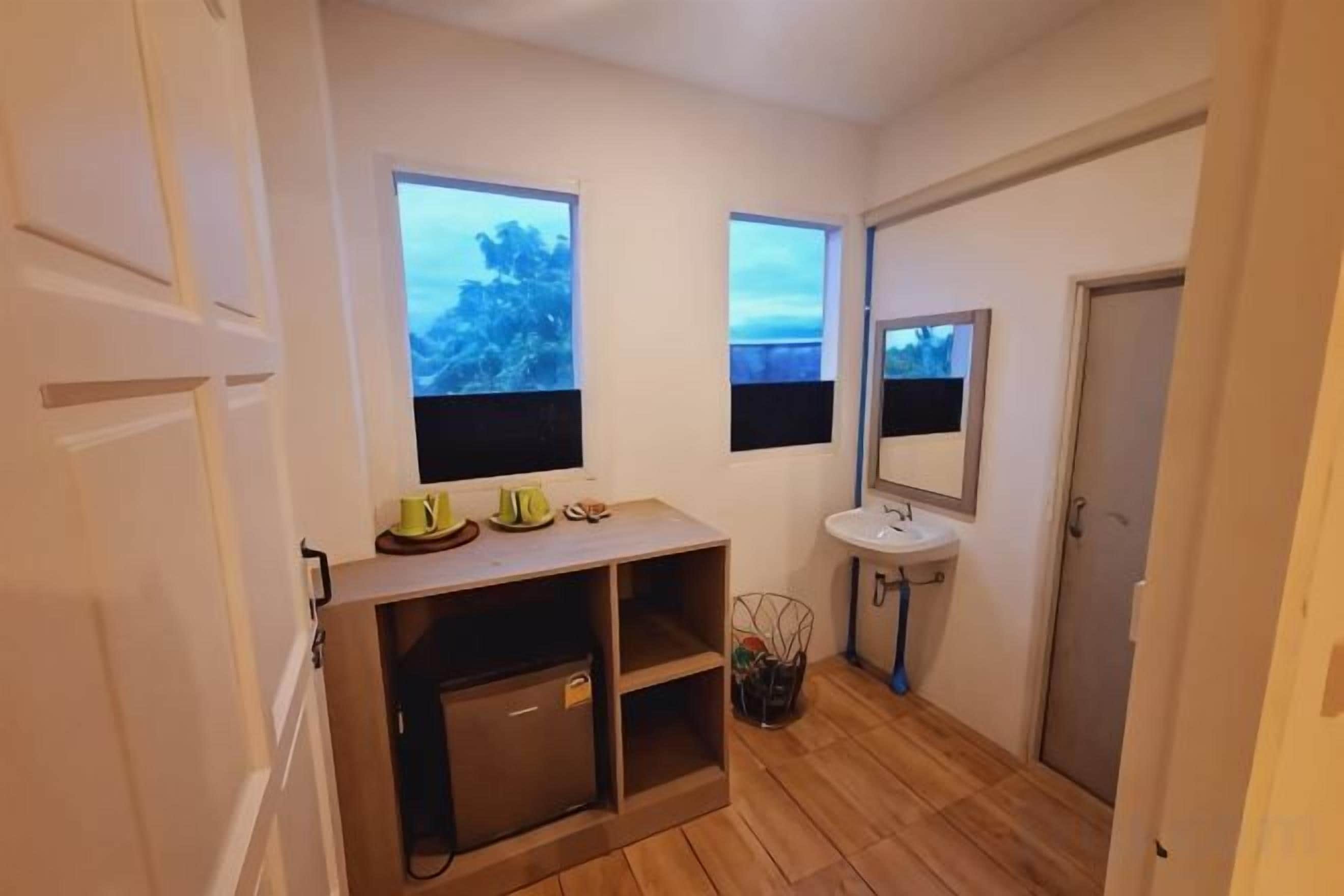 A compact bathroom with a sink, mirror, and a small cabinet. There are two windows providing natural light.