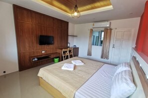 Un dormitorio con cama, escritorio, televisor y ventana con cortinas.