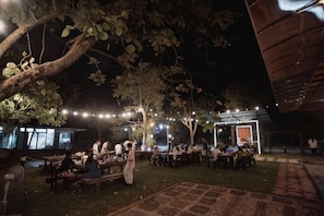 An outdoor dining area with tables and chairs, string lights, and trees. - Amphawa Horse Farm (Mueang Samut Songkhram)