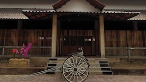 Un bâtiment traditionnel avec un toit en tuiles, des colonnes en bois et une entrée centrale.