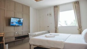 Une chambre à coucher avec un lit, un téléviseur fixé au mur, une fenêtre avec des rideaux et un luminaire au plafond.