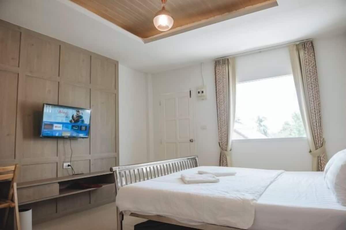 A bedroom with a bed, a television mounted on the wall, a window with curtains, and a ceiling light fixture.