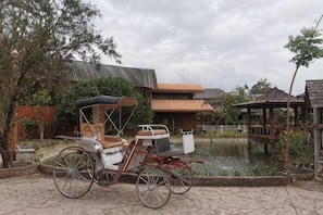 A carriage parked by a pond, a gazebo, and buildings with red-tiled roofs. - Amphawa Horse Farm (Mueang Samut Songkhram)