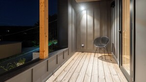 Une terrasse en bois avec une seule chaise, une porte vitrée et une source de lumière vive.