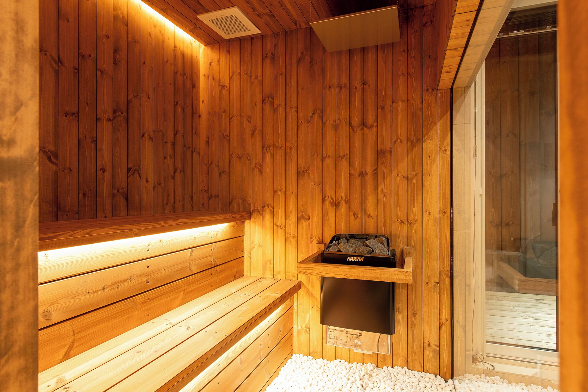 A wooden sauna with benches, a shelf with a sauna heater, and a glass door leading outside.