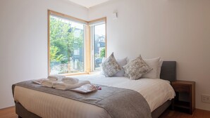 Une chambre à coucher moderne avec un grand lit, une tête de lit en bois et une vue sur l’extérieur grâce à une porte coulissante.