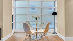 A dining area with a glass table and four white chairs, a vase with flowers, and a floor lamp.