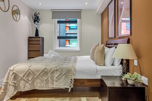 Un dormitorio con cama, mesita de noche, lámpara y ventana con persianas.