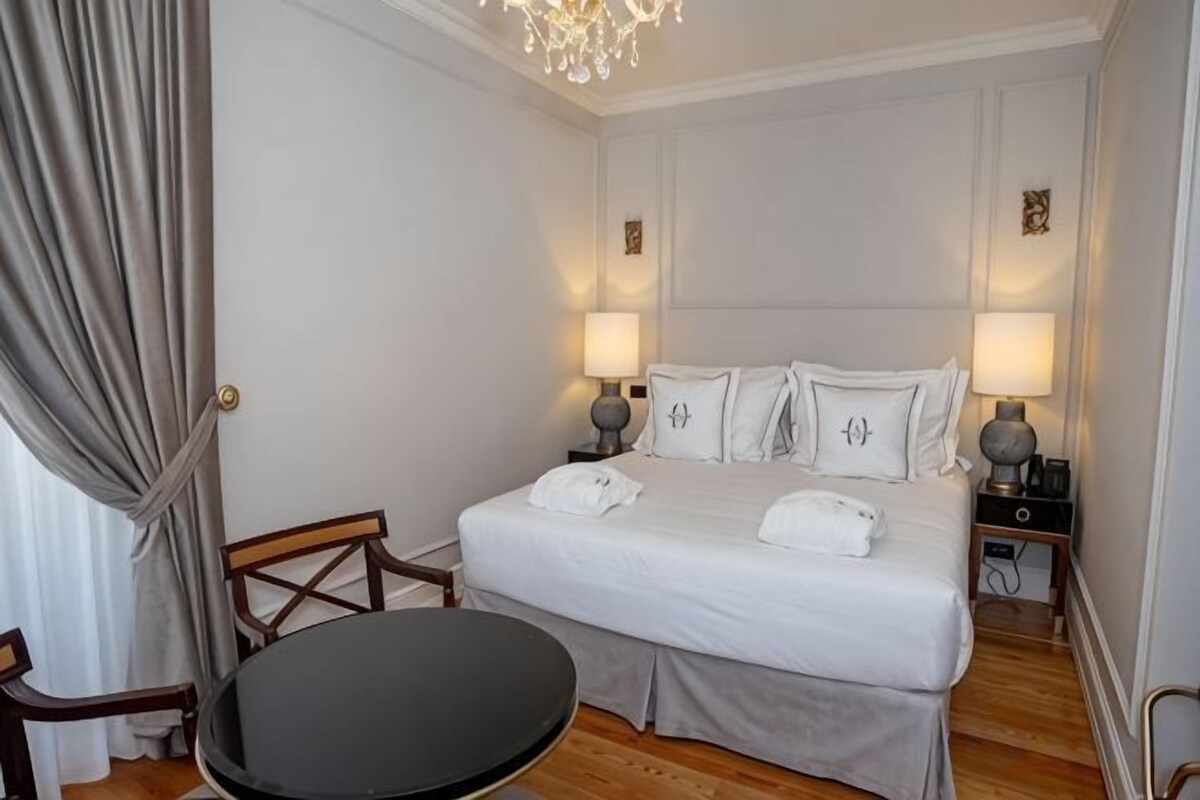 A hotel room with a bed, bedside tables, a round table, and a chandelier.