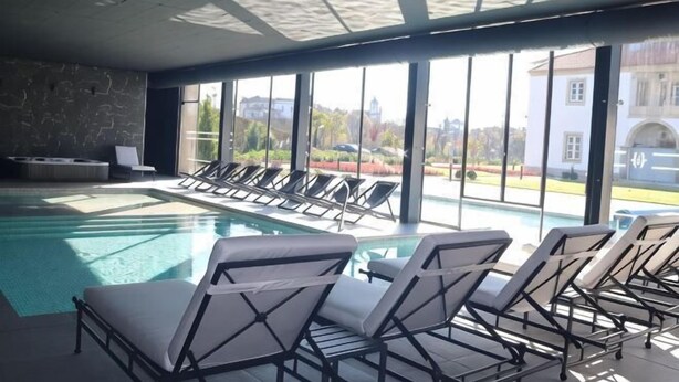 An indoor swimming pool with lounge chairs and large windows offering a view of the city. - Solar do Requeijo by Luna Hotels & Resorts (Giela)
