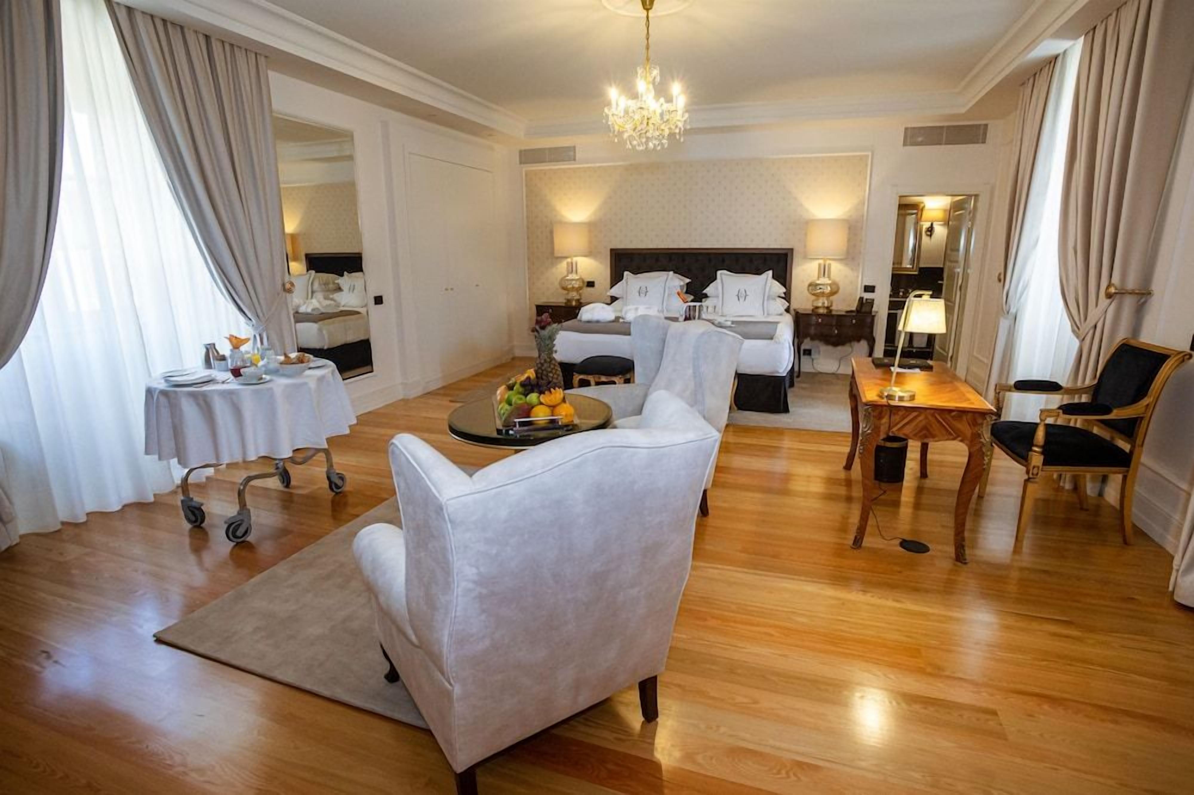 Een hotelkamer met een groot bed, een zithoek met een salontafel, een eettafel en een kroonluchter.