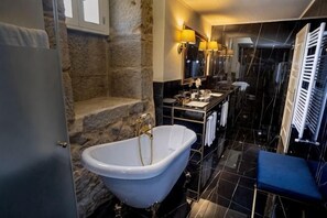 A bathroom with a freestanding bathtub, a stone wall, a mirror, and a towel rack. - Solar do Requeijo by Luna Hotels & Resorts (Giela)