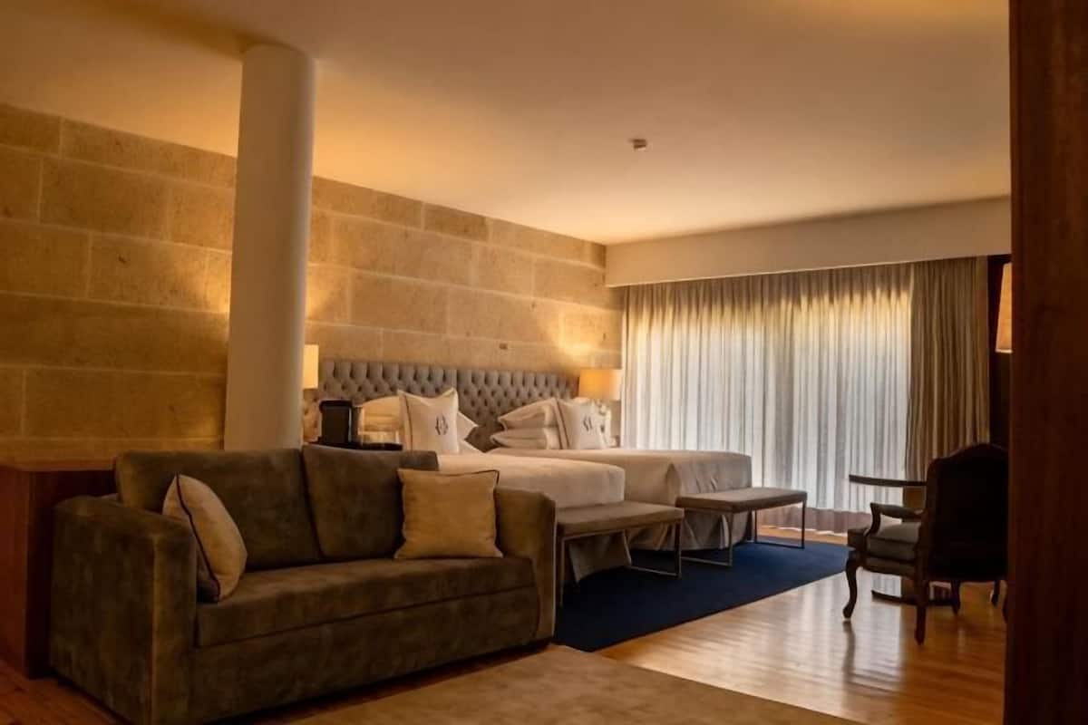 Quarto de hotel com uma cama, um sofá, uma mesinha e uma cadeira.