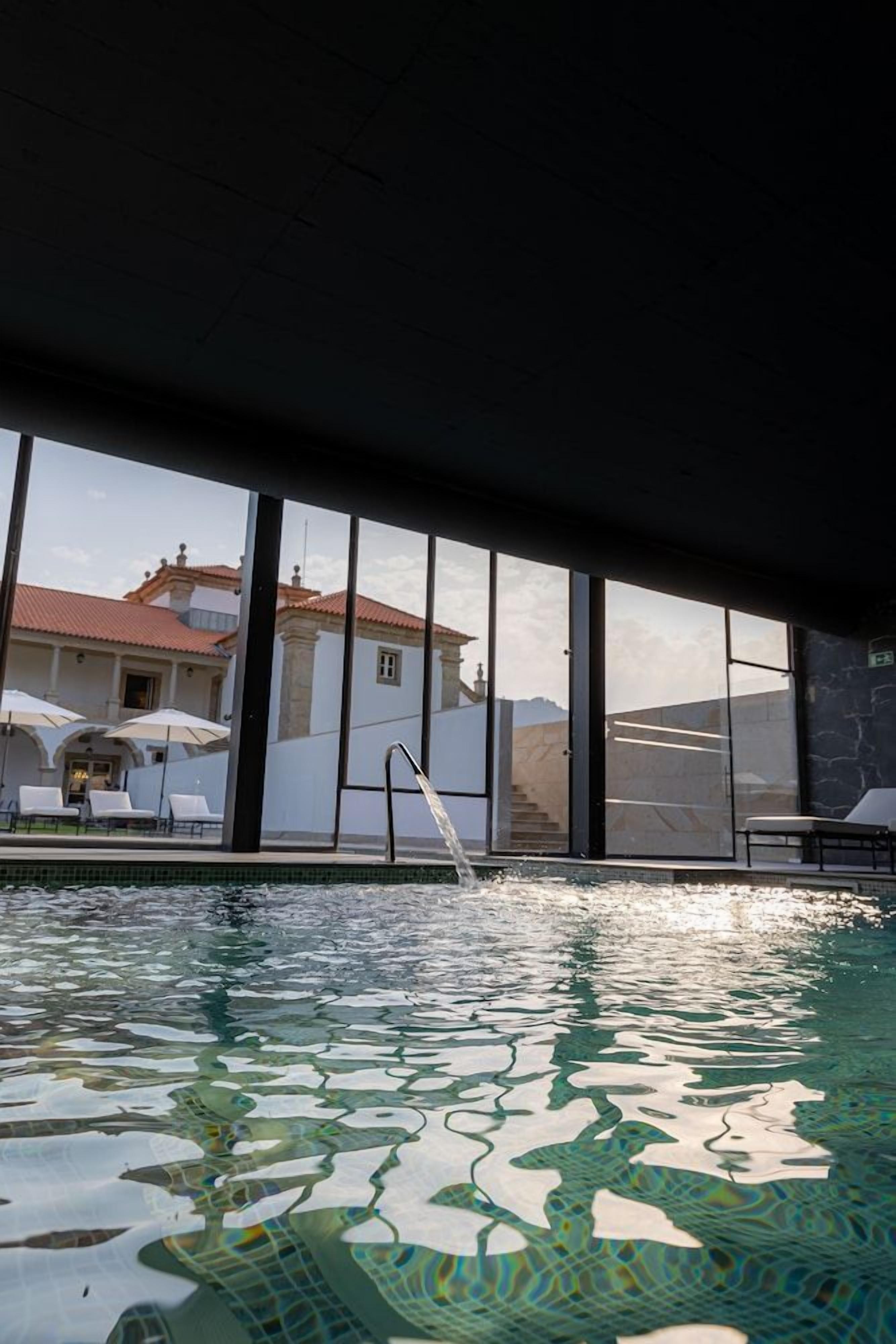 A swimming pool with clear water, a glass railing, and a view of a building with a tiled roof.