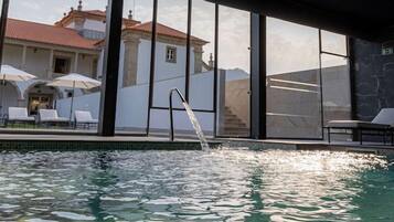 A swimming pool with clear water, a glass railing, and a view of a building with a tiled roof.