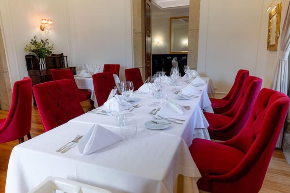 Un comedor con una larga mesa dispuesta para una comida, sillas tapizadas en rojo y un mantel blanco.