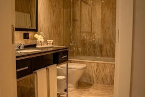 Une salle de bain avec un mur en marbre, une baignoire, des toilettes et un lavabo avec un miroir.