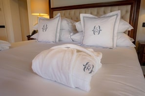 Una cama bien hecha con sábanas y almohadas blancas, un cabecero y una mesita de noche con una lámpara.