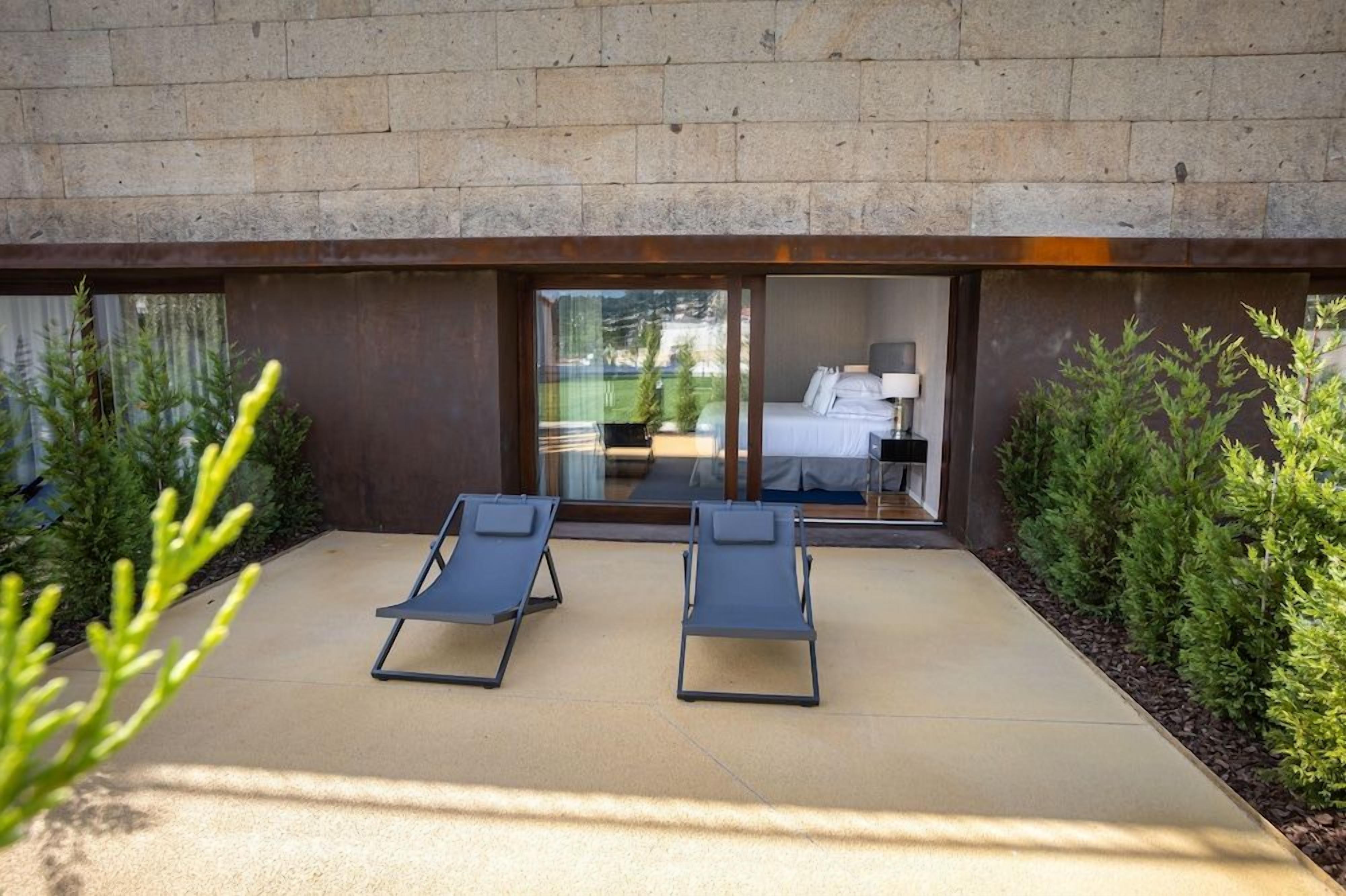 Habitación de hotel moderna con un gran ventanal corredero que da a un balcón con dos sillones de descanso.