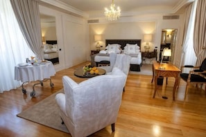 Ein Hotelzimmer mit Bett, einer Sitzecke mit Sofa und Sesseln, einem kleinen Tisch mit Obstschale und einem Chandelier.
