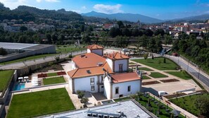 Un edificio grande con piscina, rodeado de céspedes cuidados y vistas despejadas del pueblo circundante.