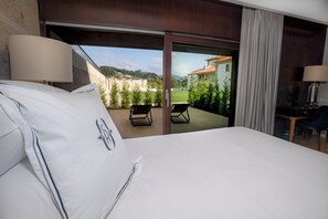 A hotel room with a large bed, a desk, and a view of a courtyard with plants and a building in the background.