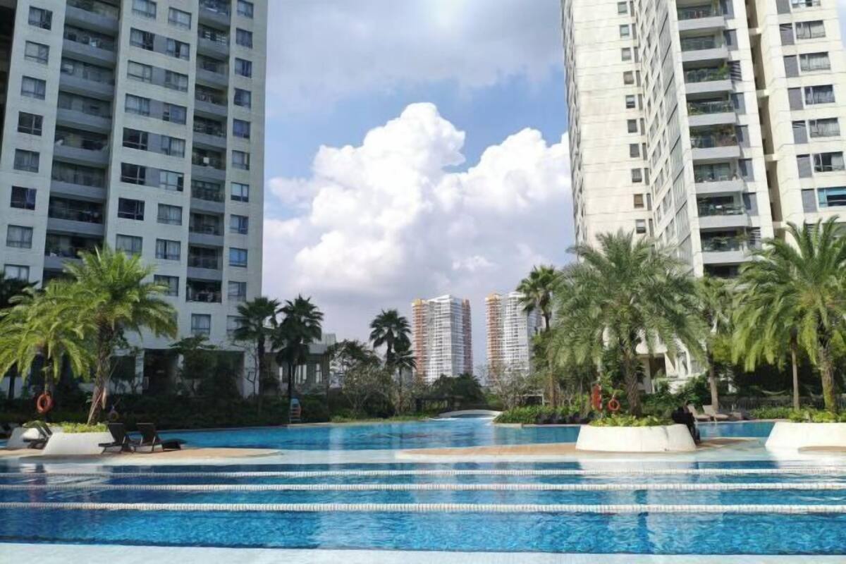 A swimming pool with multiple lanes, surrounded by palm trees and high-rise buildings.