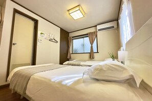 A hotel room with two beds, a window with curtains, a wall-mounted air conditioner, and a ceiling light. - Shinjuku 11 mins Private kitchen and bathroom Up to 4 guests Newly renovated Garden villa (Tokyo)