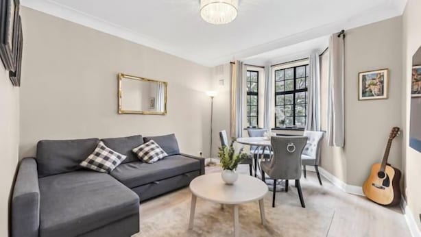 A living room with a grey sofa, a round coffee table, and a dining area with a table and chairs. - Stylish 3-Bedroom Flat in Belsize Park – Perfect for Families & Business Trips! (London)