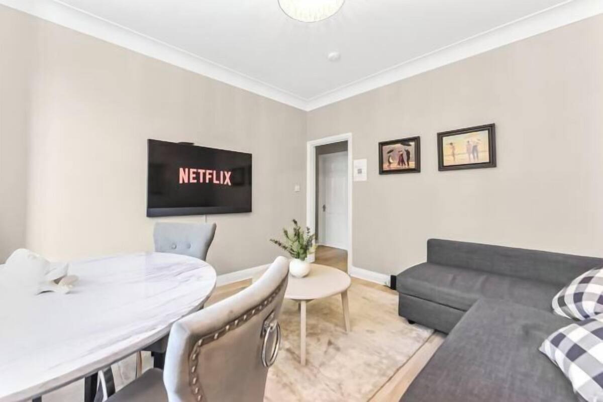 Ein Wohnzimmer mit Fernseher, einer Couch, einem Esstisch und einem Sessel.