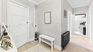 A hallway with a white bench, a radiator, and a door leading to a kitchen area. - Stylish 3-Bedroom Flat in Belsize Park – Perfect for Families & Business Trips! (London)
