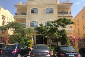A multi-story building with balconies, a gated entrance, and parked cars. - Rino Residential Apartment (New Cairo City)