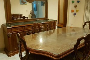 A dining area with a wooden table and chairs, a glass-top table, and a wooden cabinet with drawers. - Rino Residential Apartment (New Cairo City)