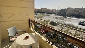 Varanda com mesa e cadeira, vista para uma rua com carros e edifícios.