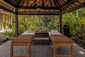 A wooden deck with two massage tables, a thatched roof, and a view of lush greenery. - Villa Kapungkur (Bali)