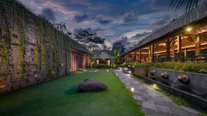 A courtyard with stone walls, a thatched-roof structure, and a pathway lined with lights. - Villa Kapungkur (Bali)