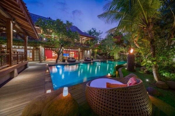 A pool area with a wooden deck, lounge chairs, and a small table with a candle. - Villa Kapungkur (Bali)