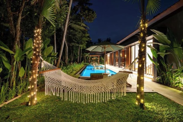 Una hamaca con luces de cadena, una piscina y un edificio con zona cubierta.