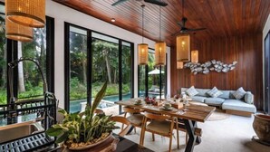 A modern dining area with a wooden table and chairs, large windows, and a view of the outdoors. - Villa Surya by BaliSuperHost (Bali)