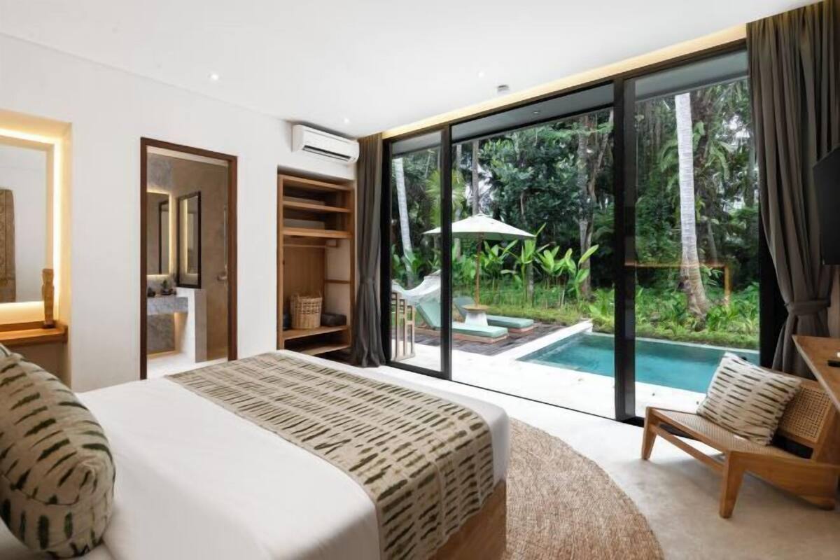 A bedroom with a bed, a chair, a TV, a wardrobe, and a sliding glass door leading to a pool.